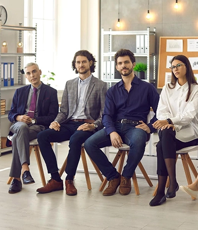 small-group-of-various-employees-sitting-for-a-coaching-session-in-a-mid-size-room a group of male and female business leaders sitting in chairs inside of a modern learning space are all attentive and listening to someone speaking behind the camera