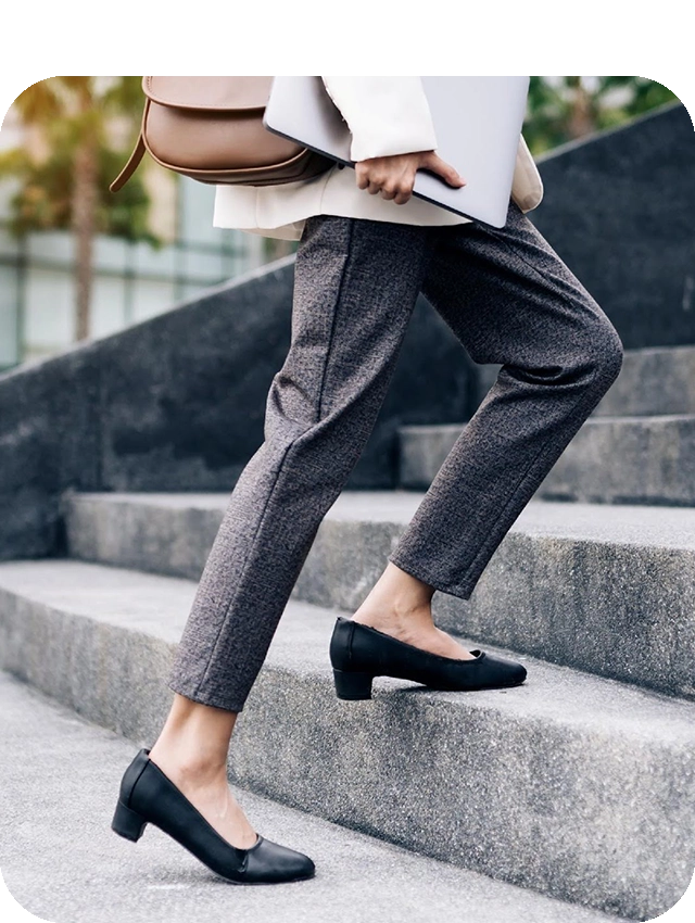 young-woman-walking-up-the-stairs-in-high-heels-holding-a-laptop a shot of women legs walking up a flight of concrete steps. The woman is wearing a dress pants and a white blazer, while holding a laptop and purse in her arms